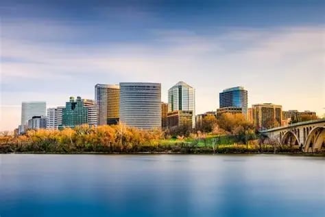 Skyline of modern office buildings along a river during golden hour, with autumn trees and a bridge visible