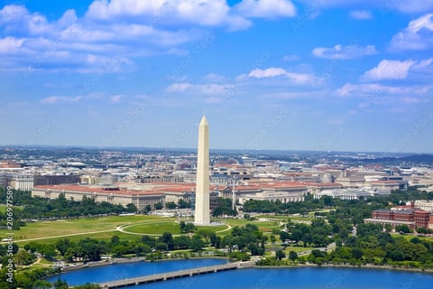Aerial view of Washington Monument with Potomac River, green parkland, and city buildings under blue sky
