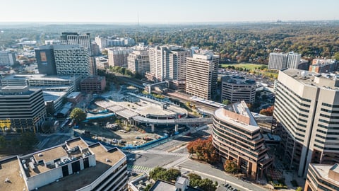 Aerial view of a sprawling urban cityscape with high-rise buildings, highways, and green parks under a clear sky