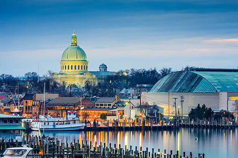 Golden dome capitol building reflected in calm waterfront with docked boats and historic buildings at dusk
